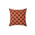 A square throw pillow with an orange background and a repeating black cat face pattern,.