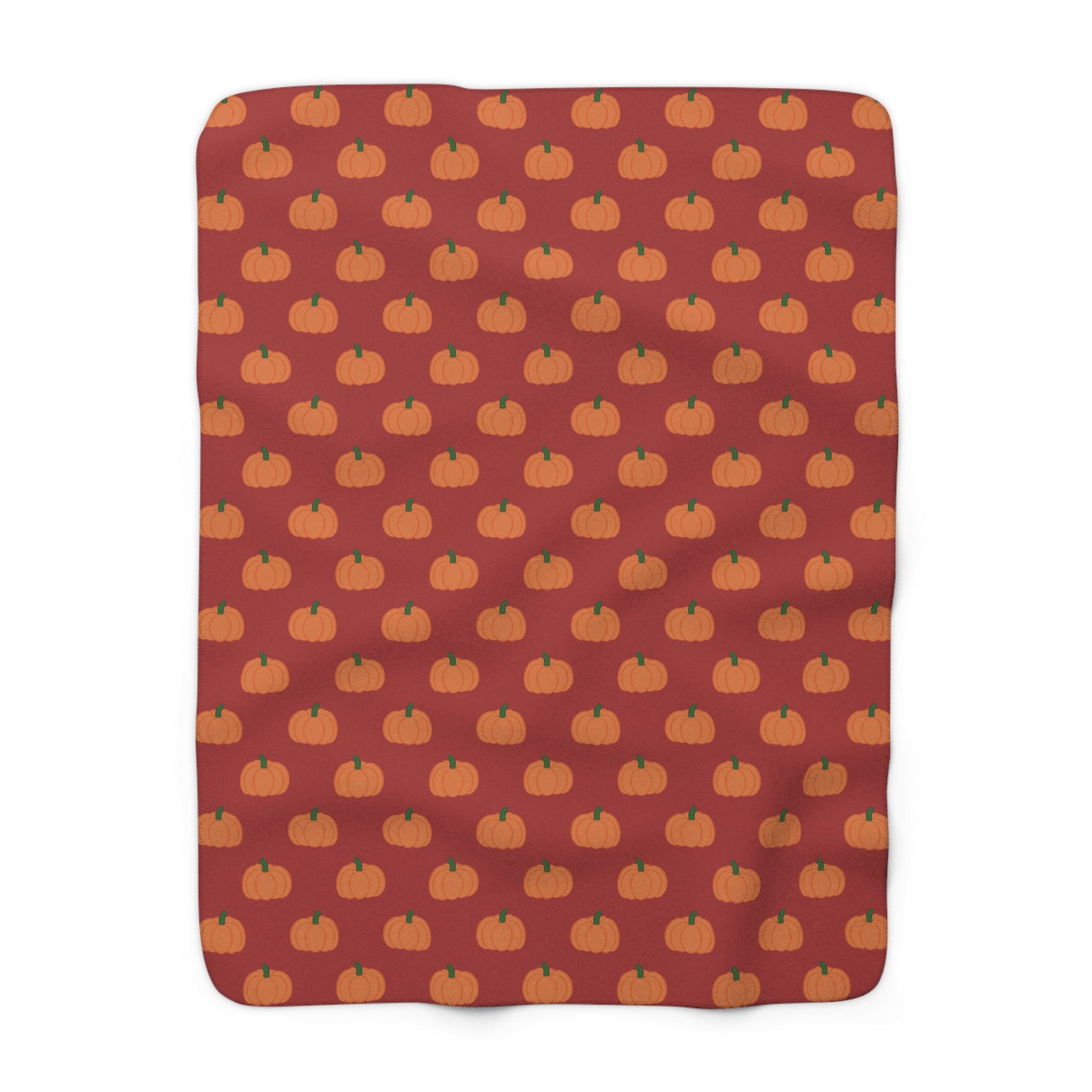 A rectangular blanket with rounded corners featuring a repeating pattern of small orange pumpkins on a dark red background.